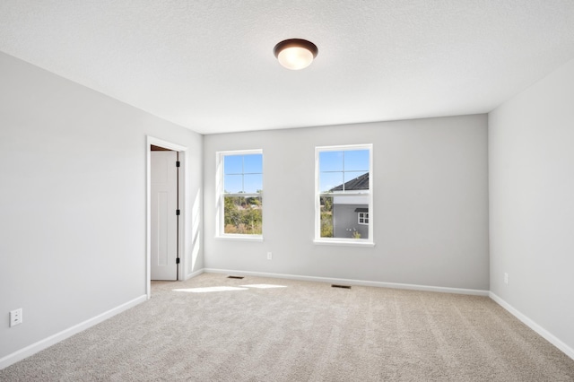 spare room with a textured ceiling, carpet, visible vents, and baseboards