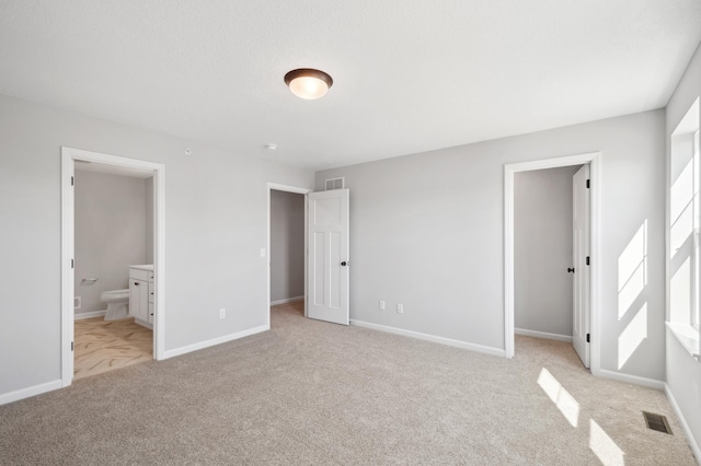 unfurnished bedroom featuring light carpet, a spacious closet, visible vents, and baseboards