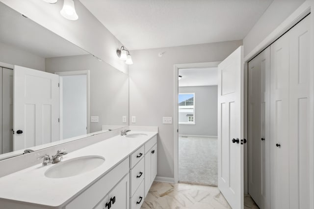 full bathroom with marble finish floor, a sink, baseboards, and double vanity