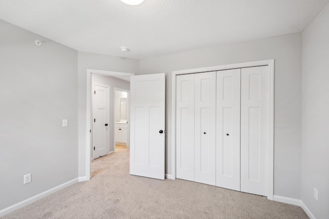 unfurnished bedroom featuring light carpet, a textured ceiling, baseboards, and a closet