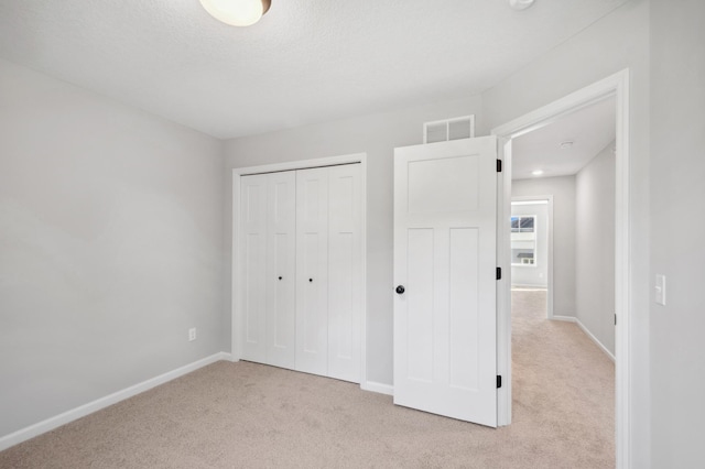 unfurnished bedroom featuring a closet, visible vents, light carpet, a textured ceiling, and baseboards