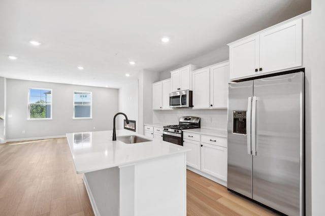 kitchen with a center island with sink, light wood finished floors, tasteful backsplash, appliances with stainless steel finishes, and a sink