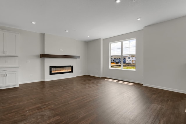 unfurnished living room with recessed lighting, baseboards, dark wood-type flooring, and a glass covered fireplace