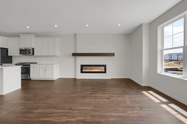 unfurnished living room featuring dark wood finished floors, a glass covered fireplace, a wealth of natural light, and baseboards