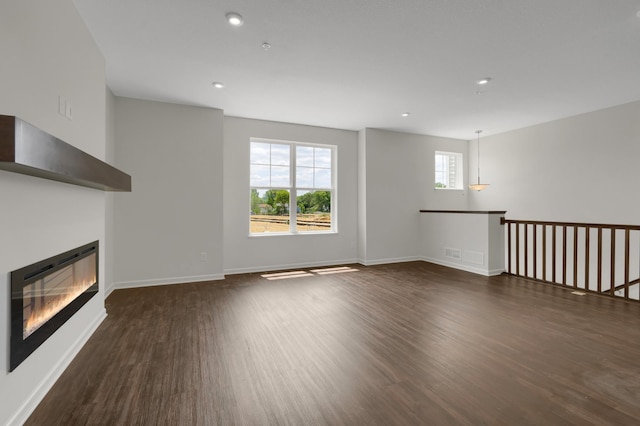 unfurnished living room featuring recessed lighting, baseboards, dark wood finished floors, and a glass covered fireplace