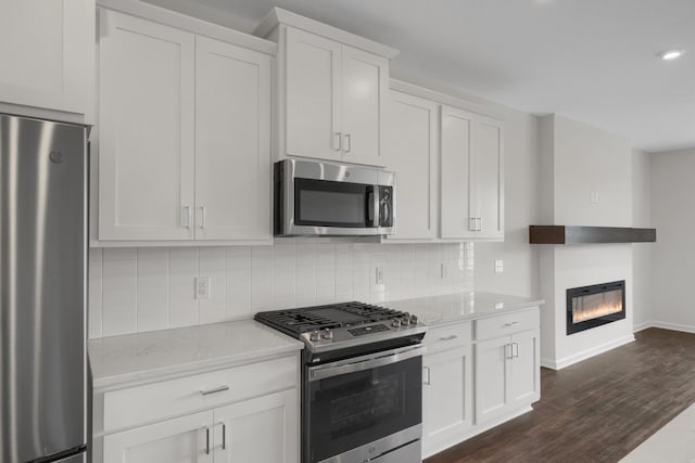 kitchen featuring white cabinets, decorative backsplash, light stone counters, appliances with stainless steel finishes, and dark wood-type flooring