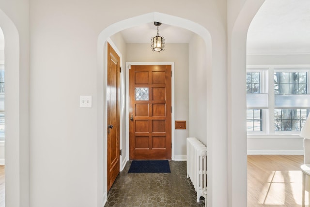 foyer entrance with arched walkways, radiator, and baseboards