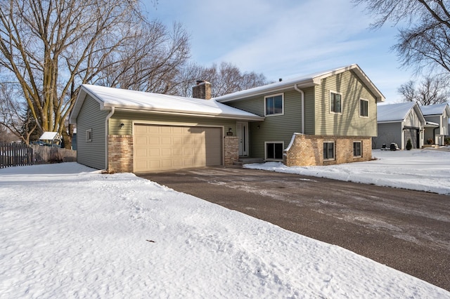 split level home with a garage, brick siding, a chimney, and aphalt driveway