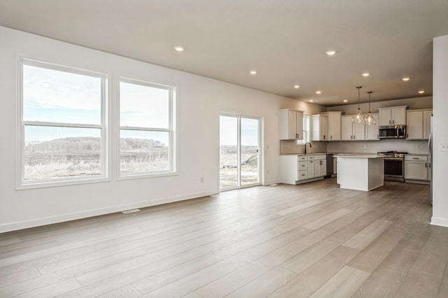 unfurnished living room featuring light wood finished floors, baseboards, a sink, and recessed lighting