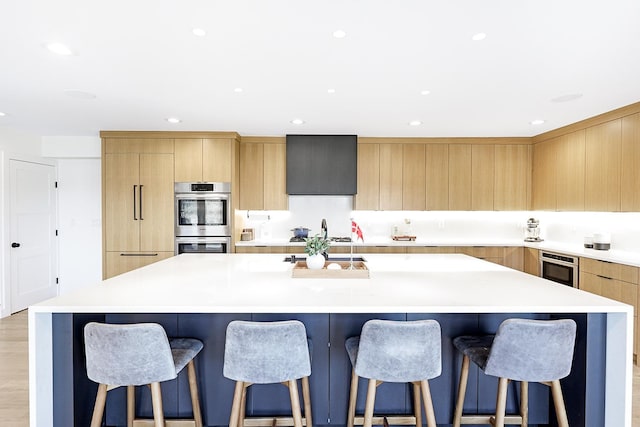 kitchen featuring stainless steel double oven, light countertops, modern cabinets, cooktop, and a large island with sink