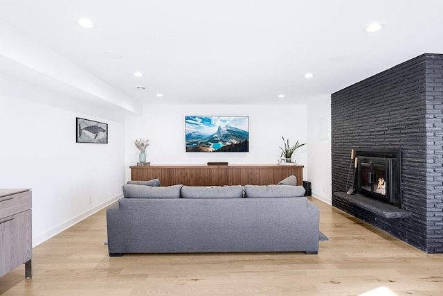 living room with baseboards, recessed lighting, a brick fireplace, and light wood-style floors