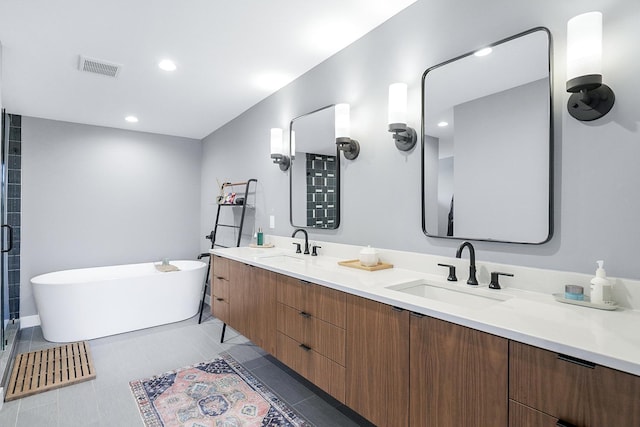 full bathroom with double vanity, a freestanding tub, visible vents, and a sink