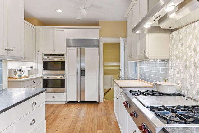 4943 Dupont Ave S, Minneapolis, MN 55419 - kitchen with wall chimney range hood, stainless steel appliances, white cabinetry, light wood-style flooring, and ceiling fan