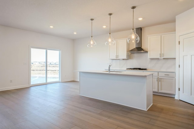 kitchen with a kitchen island with sink, white cabinetry, light countertops, wall chimney range hood, and pendant lighting