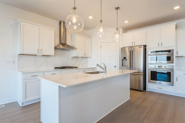 kitchen featuring stainless steel appliances, a sink, hanging light fixtures, light countertops, and wall chimney exhaust hood