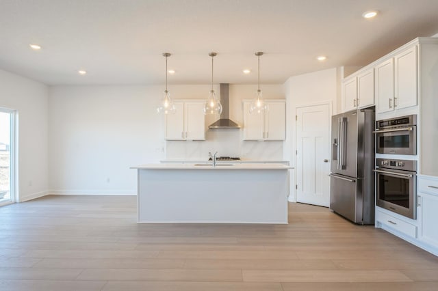 kitchen featuring wall chimney exhaust hood, appliances with stainless steel finishes, hanging light fixtures, and white cabinetry