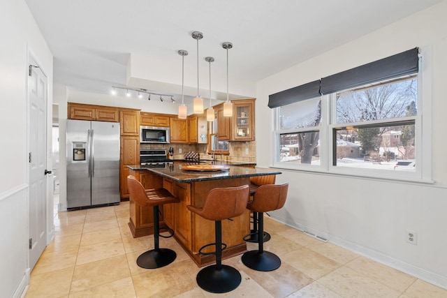 kitchen featuring a breakfast bar area, brown cabinetry, decorative backsplash, appliances with stainless steel finishes, and pendant lighting