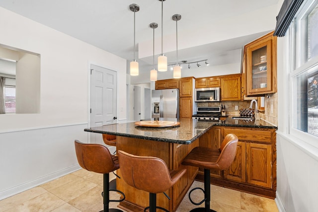 kitchen featuring a breakfast bar, decorative backsplash, appliances with stainless steel finishes, brown cabinetry, and a sink