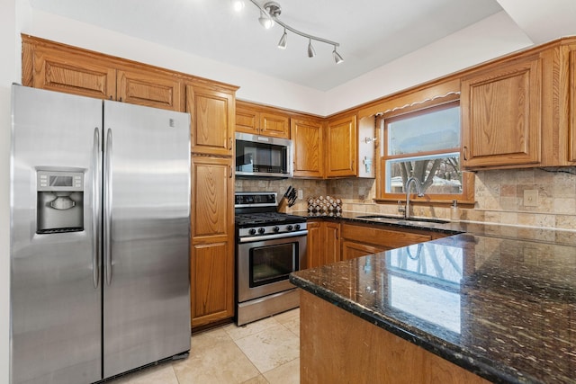 kitchen with dark stone countertops, brown cabinetry, a sink, decorative backsplash, and appliances with stainless steel finishes