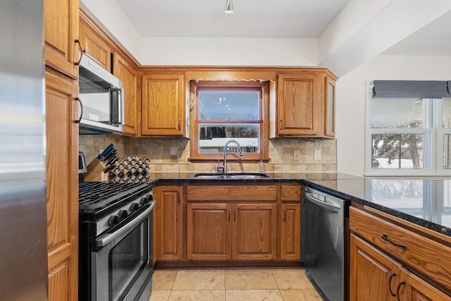 kitchen with backsplash, dark stone countertops, brown cabinets, stainless steel appliances, and a sink