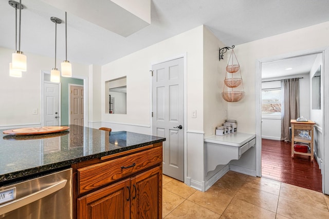 kitchen with dark stone countertops, light tile patterned floors, brown cabinets, and pendant lighting