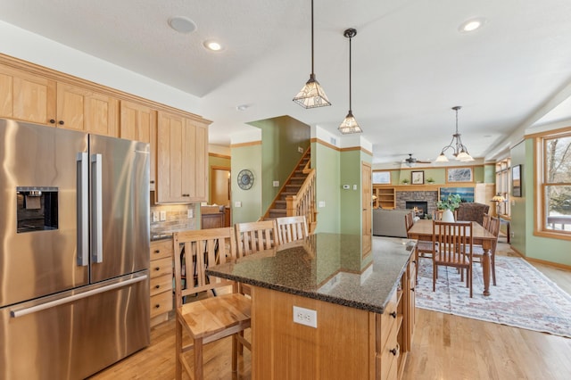 kitchen featuring dark stone counters, a kitchen island, open floor plan, a fireplace, and high end fridge