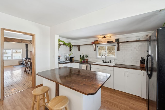 kitchen with dark countertops, freestanding refrigerator, white cabinets, a sink, and a kitchen breakfast bar