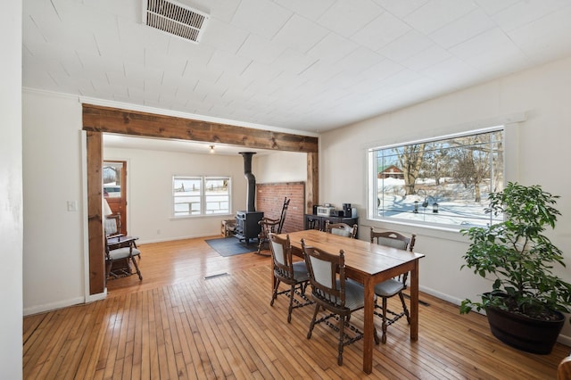 dining area featuring a wood stove, visible vents, baseboards, and light wood finished floors