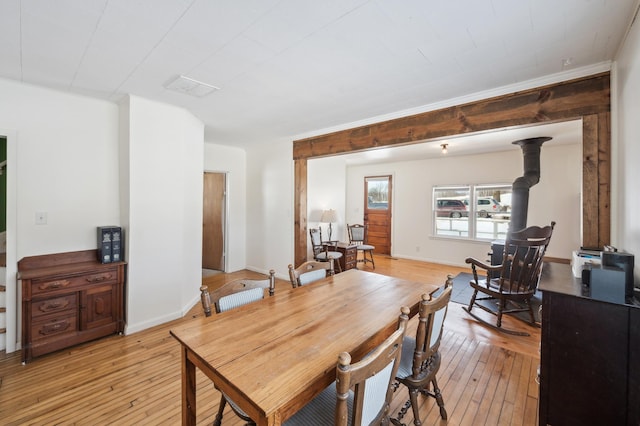 dining space featuring a wood stove, visible vents, light wood-style flooring, and baseboards