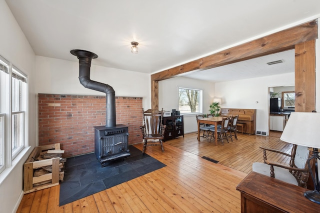 living area featuring visible vents, beam ceiling, wood finished floors, and a wood stove