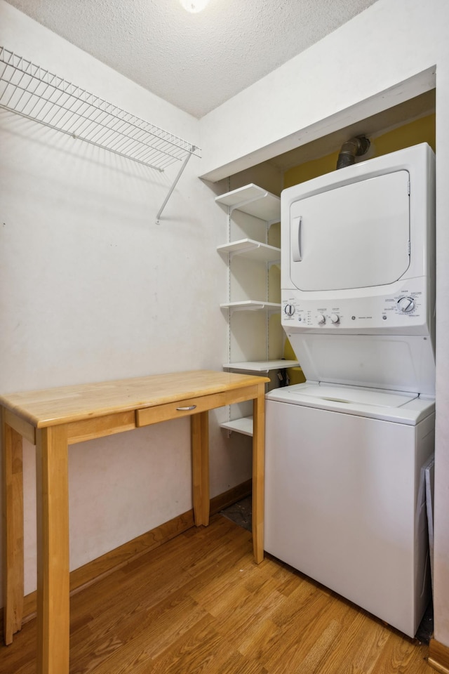 laundry area featuring stacked washing maching and dryer, a textured ceiling, laundry area, and light wood-style flooring