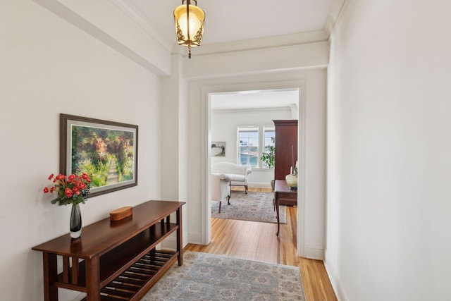 hallway with baseboards, light wood-type flooring, and crown molding