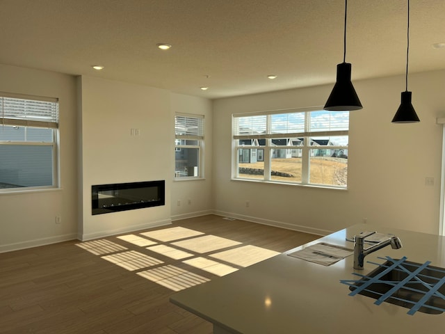 unfurnished living room featuring a glass covered fireplace, baseboards, recessed lighting, and wood finished floors