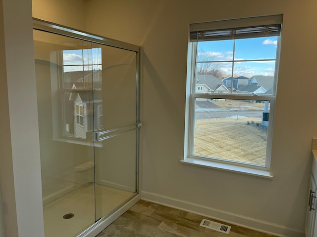 bathroom featuring a wealth of natural light, a shower stall, visible vents, and baseboards