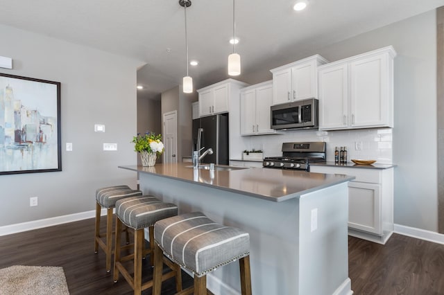 kitchen with decorative light fixtures, stainless steel appliances, a sink, white cabinetry, and a center island with sink