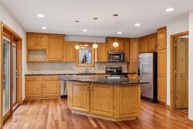 kitchen with light wood finished floors, dark stone counters, a sink, appliances with stainless steel finishes, and a center island