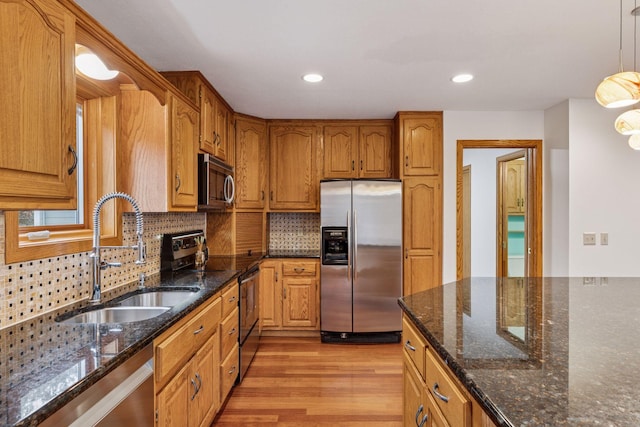 kitchen featuring light wood finished floors, decorative backsplash, brown cabinetry, stainless steel appliances, and a sink