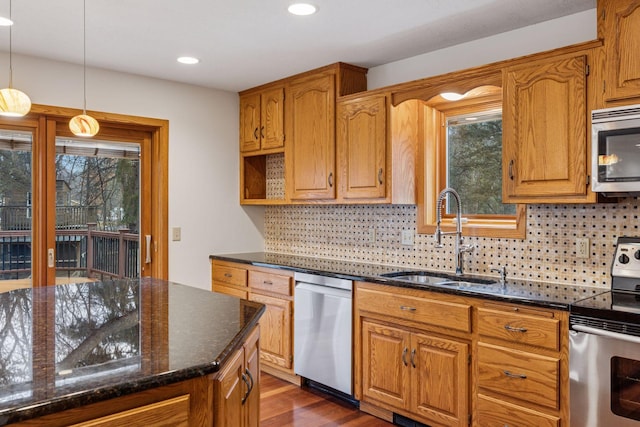 kitchen with dark stone countertops, a sink, stainless steel appliances, dark wood-type flooring, and decorative light fixtures