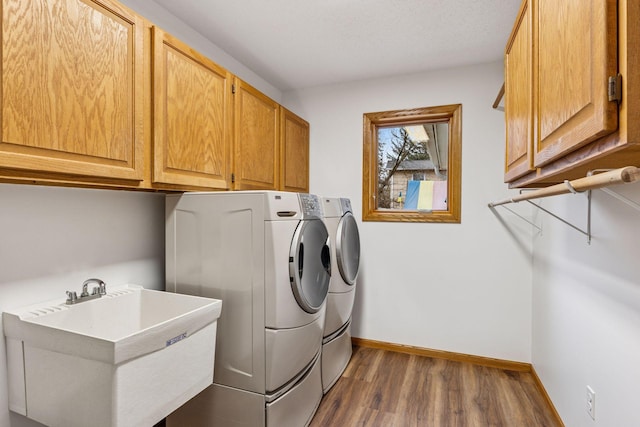 laundry room with a sink, baseboards, washer and clothes dryer, cabinet space, and dark wood-style flooring