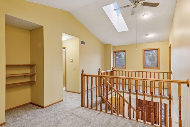 hallway with visible vents, baseboards, carpet floors, an upstairs landing, and vaulted ceiling with skylight