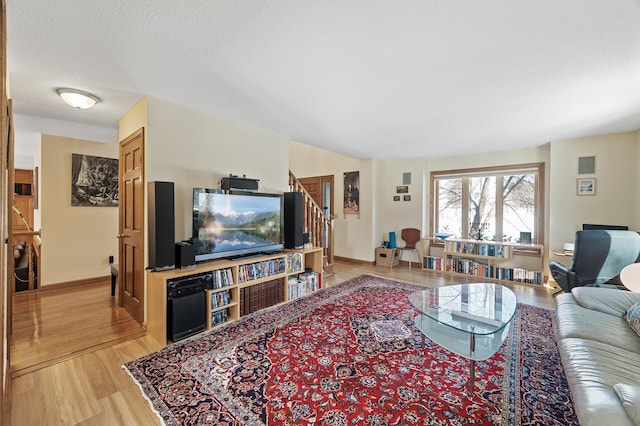 living room with light wood-type flooring, stairs, baseboards, and a textured ceiling