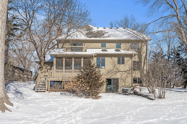 snow covered back of property featuring a balcony, a sunroom, and stairway