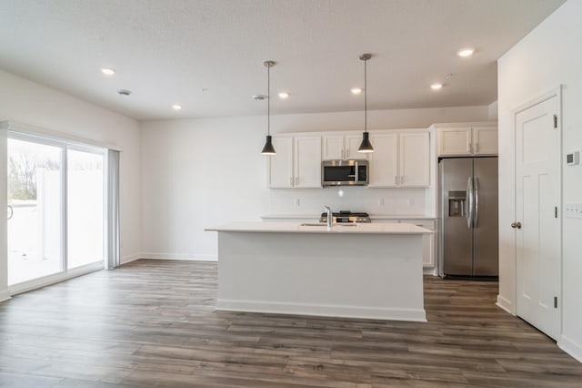 kitchen featuring light countertops, appliances with stainless steel finishes, an island with sink, and pendant lighting