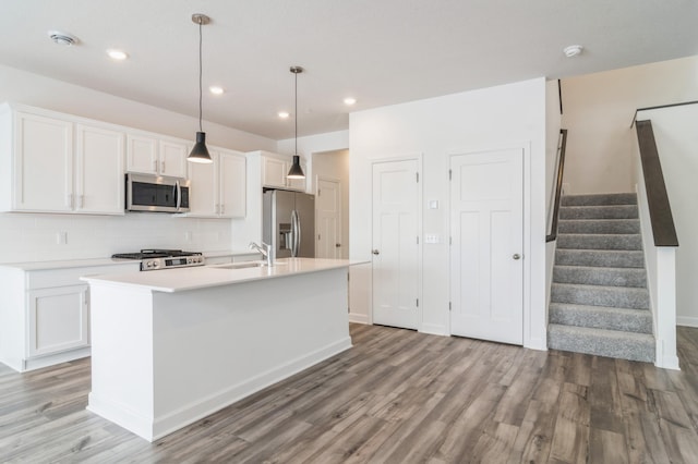 kitchen featuring a center island with sink, appliances with stainless steel finishes, hanging light fixtures, light countertops, and white cabinetry