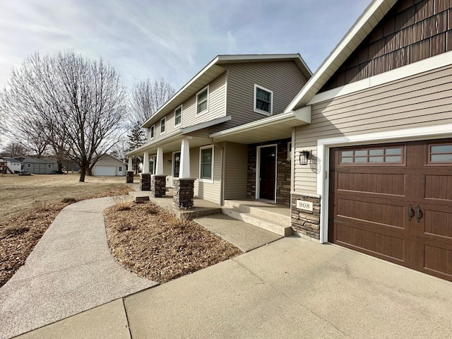 view of front of house with a garage, stone siding, a porch, and driveway