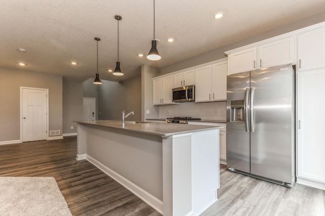 kitchen featuring a kitchen island with sink, stainless steel appliances, a sink, white cabinets, and decorative light fixtures