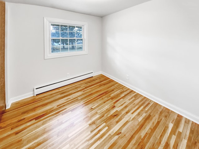 empty room featuring a baseboard heating unit, light wood-style flooring, and baseboards