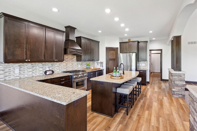 4680 Spruce Way, Medina, MN 55359 - kitchen featuring appliances with stainless steel finishes, custom exhaust hood, light wood-style flooring, light stone counters, and dark brown cabinets