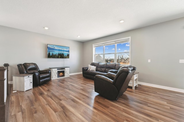 living room with a textured ceiling, recessed lighting, wood finished floors, baseboards, and a lit fireplace