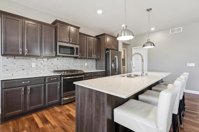 kitchen with visible vents, decorative backsplash, dark wood finished floors, stainless steel appliances, and a sink